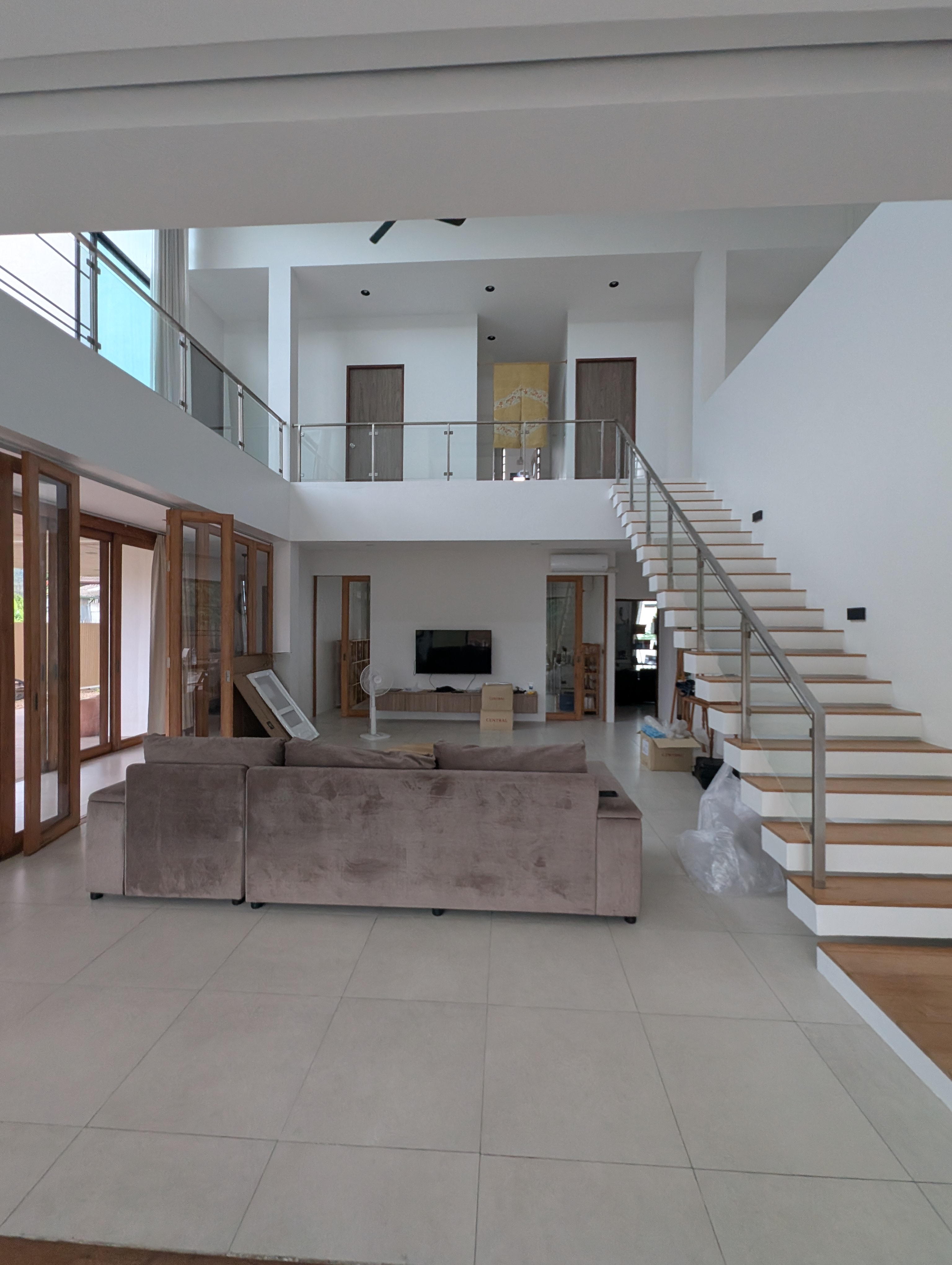 Double-height living room with a couch, large windows and an open staircase